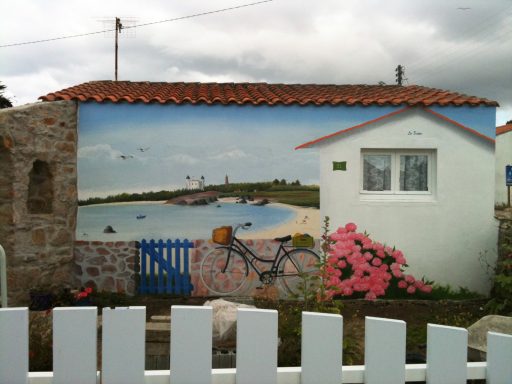 Maison avec une fresque murale de paysage maritime et un vélo devant des fleurs.