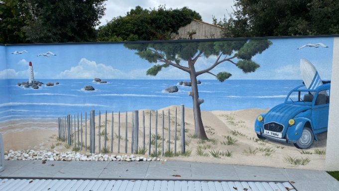 Peinture trompe oeil extérieure dans jardin avec piscine Fresque représentant une plage avec une voiture bleue et un voilier à l'horizon.