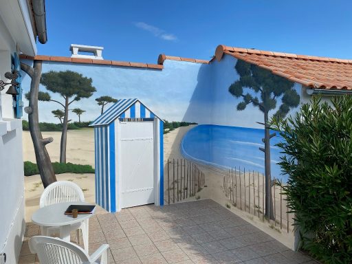 Cabane de plage peinte, vue sur mer et arbres, ambiance ensoleillée.