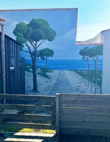 Fresque Murale représentant un chemin sablonneux menant à la mer, avec des pins au loin.