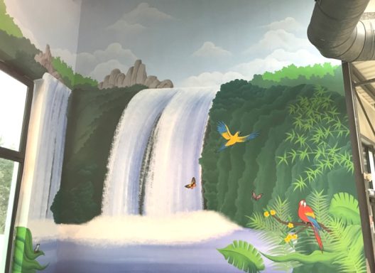 Fresque murale représentant des cascades entourées de verdure et d'oiseaux colorés.